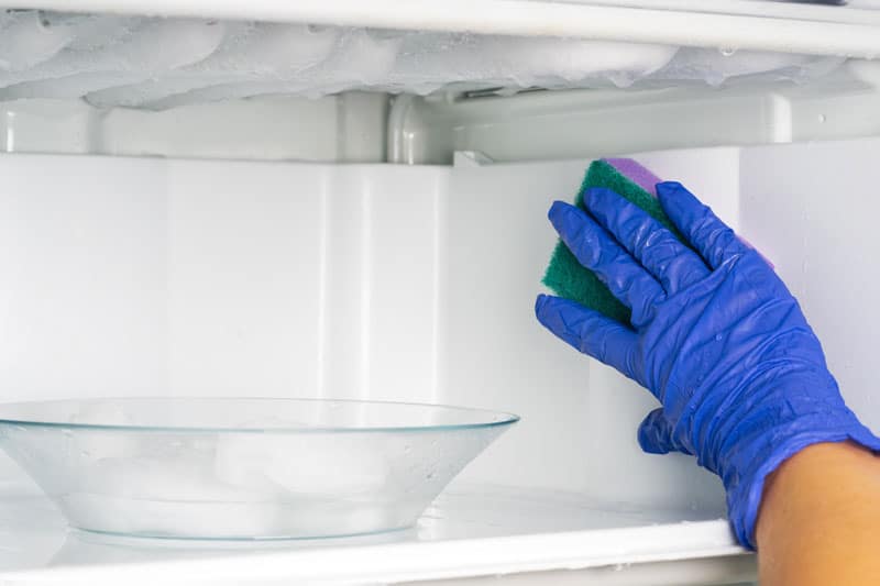 Personne qui dégivre son frigo avec une éponge
