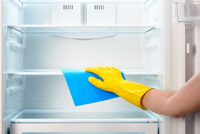 Personne qui nettoie l'intérieur d'un frigo avec des gants et un linge propre